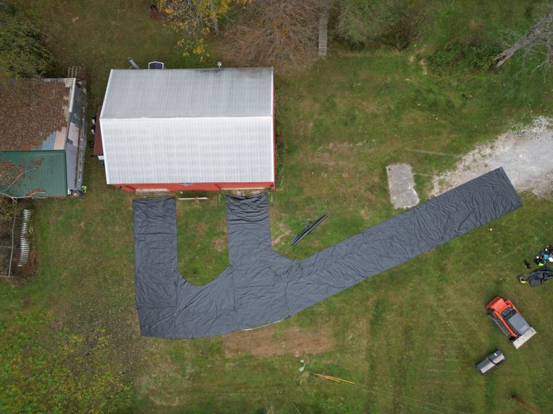 Drone view of geotextile fabric laid out for a new driveway beside a white barn