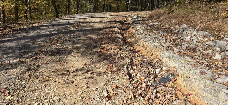 Erosion cut along the edge of a steep gravel driveway before the work