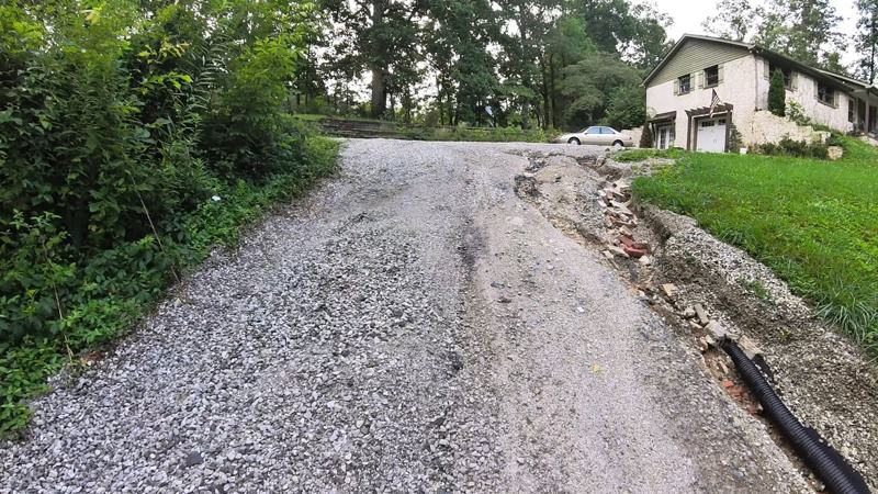 A washed-out gravel driveway with ruts and loose stone before recovery