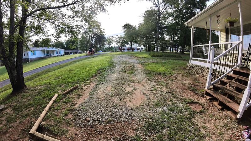 A worn gravel driveway with bare dirt patches beside a house