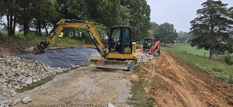 An excavator setting rock on geotextile fabric