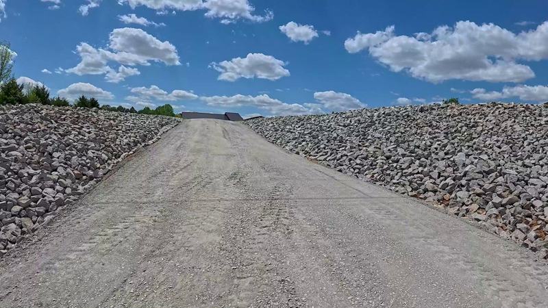 A freshly graded and compacted gravel driveway with rock-lined ditches on both sides